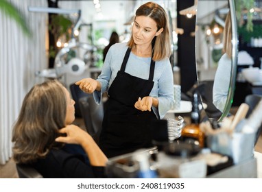 Friendly young woman hairdresser discussing haircut with aged female client sitting in chair in hairdressing salon. - Powered by Shutterstock