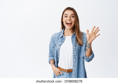 Friendly Young Woman Say Hi And Wave Hand Cheerful, Smiling At Camera To Greet You, Standing Against White Background