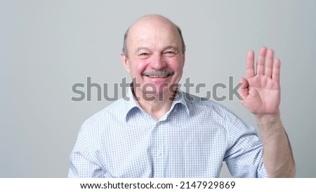 Friendly-looking attractive european man waiving hand in hello gesture while smiling cheerfully. Host is glad to welcome his guests or friends