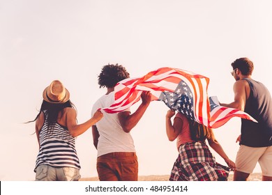 Friends with American flag. Rear view of four young people carrying american flag while running outdoors - Powered by Shutterstock