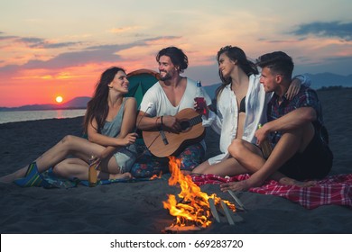 Friends Around The Fire In Sunset On Beach