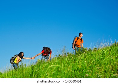 Friends with backpacks on climbing the summer hill
