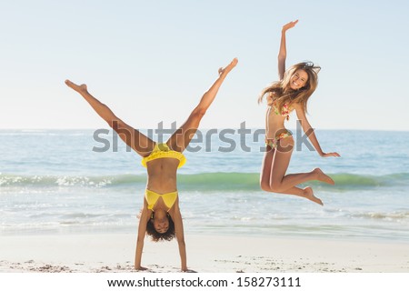 Friends in bikinis jumping and doing handstand on beach on holidays