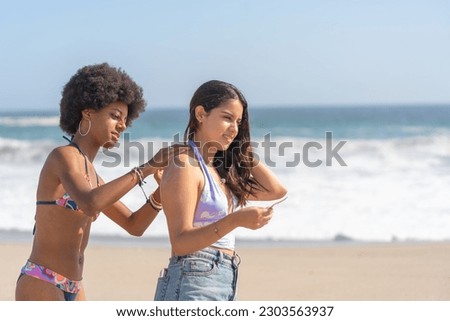 Friends in bikinis putting sunscreen on their backs, on the beach