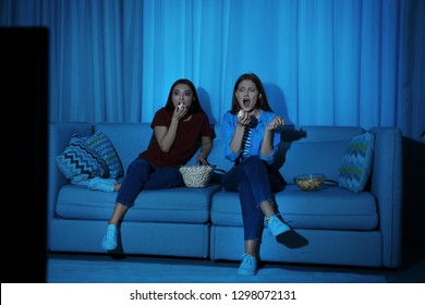 Friends With Bowl Of Popcorn Watching TV Together On Sofa In Dark Living Room