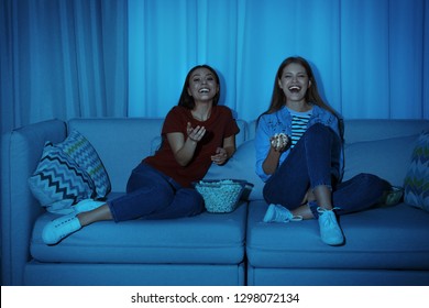 Friends With Bowl Of Popcorn Watching TV Together On Sofa In Dark Living Room