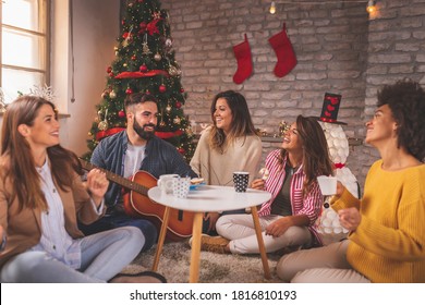 Friends Celebrating Christmas At Home, Eating Christmas Cookies, Drinking Coffee, Playing The Guitar And Singing Christmas Songs