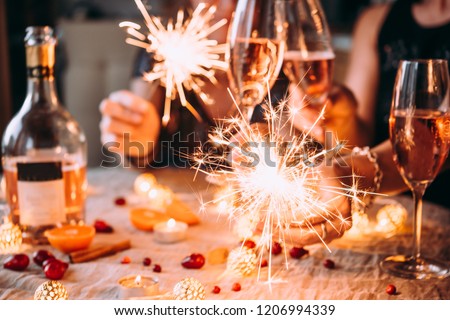 Friends celebrating Christmas or New Year eve party with Bengal lights and rose champagne.