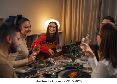 friends celebrating singing and playing guitar at home dinner party