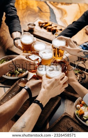 Friends cheering beer glasses on wooden table covered with delicious food - Top view of people having dinner party at bar restaurant - Food and beverage lifestyle concept