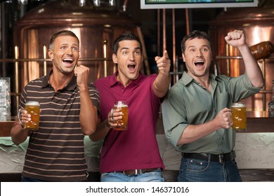 Friends Cheering. Three Happy Soccer Fans Drinking Beer At The Pub