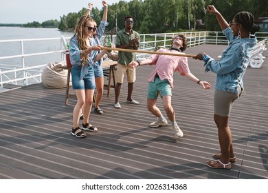 Friends Cheering For Young Man Bending Backwards To Walk Under Vertical Bar Playing Limbo