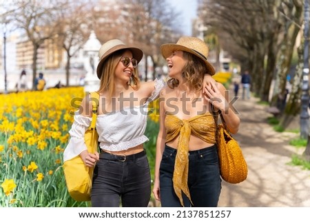 Friends in the city with straw hats walking and smiling next to some beautiful yellow flowers, enjoying spring on vacation