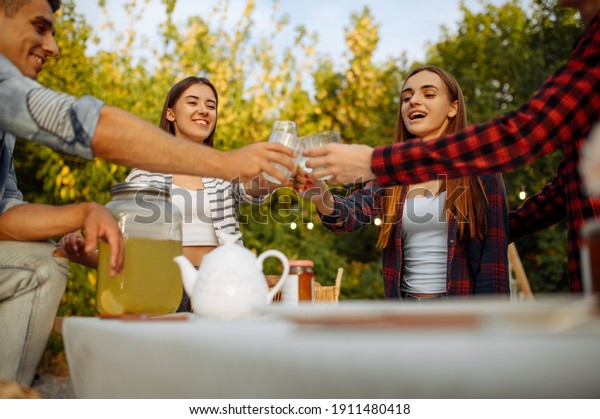 Friends clink\
glasses at table, picnic at\
camping