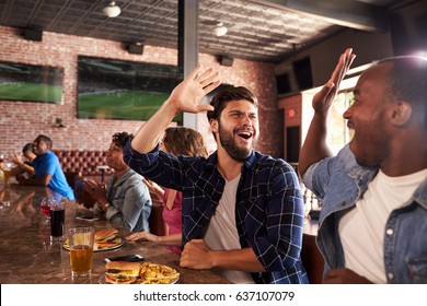 Friends At Counter In Sports Bar Watch Game And Celebrate