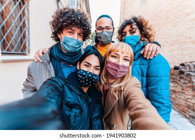 Friends covered by facemasks taking a selfie outside in the city - New normal lifestyle concept with young people having fun together outdoors on vacation