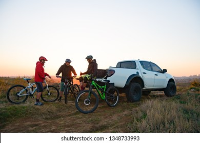 Friends Cyclists Resting Near The Pickup Off Road Truck After Enduro Bike Riding In The Mountains At Warm Autumn Sunset. MTB Adventure And Car Travel Concept.