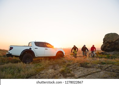 Friends Cyclists Riding Enduro Bikes in the Mountains in front of the Pickup Off Road Truck at Warm Autumn Sunset. MTB Adventure and Car Travel Concept. - Powered by Shutterstock