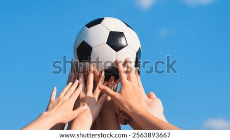 Friends demonstrating teamwork and unity by raising a soccer ball above their heads against a clear blue sky