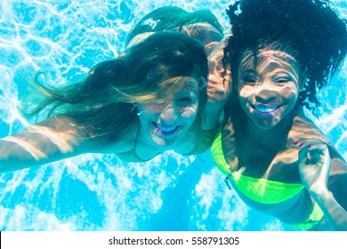 Friends diving underwater in swimming pool, black and white girl