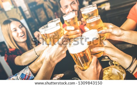Friends drinking beer at brewery bar restaurant on weekend - Friendship concept with young people having fun together toasting brew pint on happy hour at pub - Focus on glass - Bright contrast filter