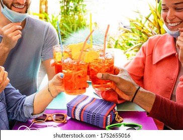 Friends drinking coktail  in a restaurant bar outside in summer days with face mask on to be protected from coronavirus - Happy people cheering with spritz and having fun 