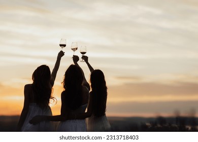 Friends drinking wine at sunset, back view. Silhouettes of people on nature. Copy space. - Shutterstock ID 2313718403