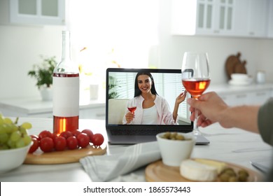 Friends drinking wine while communicating through online video conference in kitchen. Social distancing during coronavirus pandemic