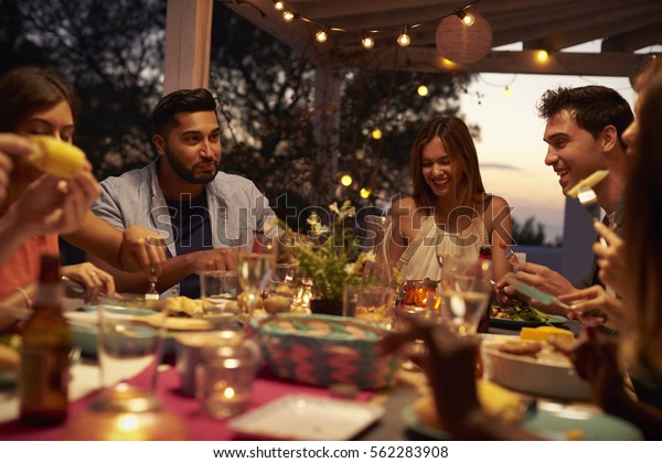 Friends eat and talk at a dinner party on a patio,\
close up