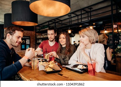 Friends Eating French Fries And Hamburgers Together At Outdoor Restaurant Under Summer Sun.