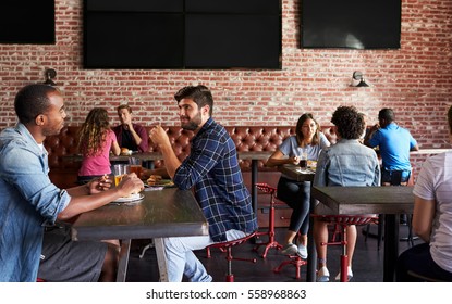 Friends Eating Out In Sports Bar With Screens In Background