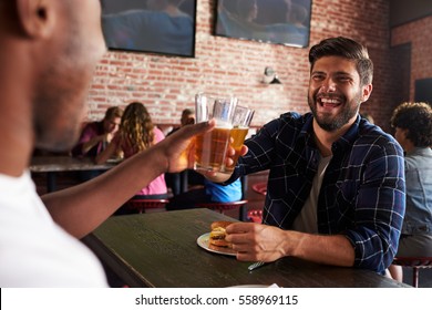 Friends Eating Out In Sports Bar With Screens In Background