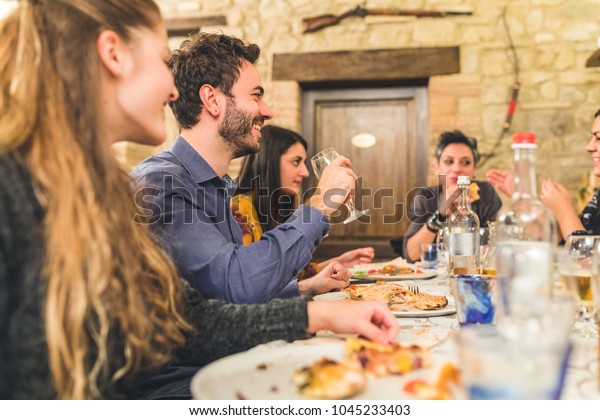 Friends eating pizza together and having\
fun. Group of friends together at restaurant enjoying proper\
Italian pizzas. Friendship and Italian food\
concepts.