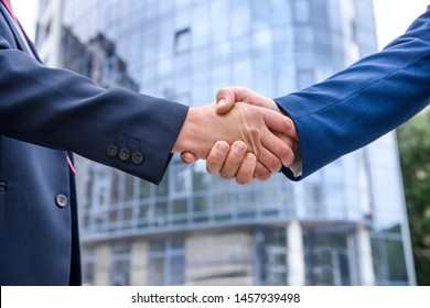 Friends in elegant business suits handshaking outdoors