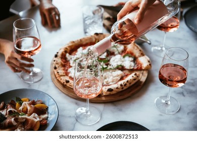 Friends enjoy a dinner party with pizza and rose wine in a bar or a restaurant.
