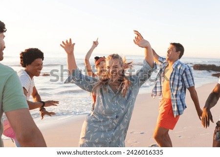 Friends enjoy a lively beach party at sunset. The group's laughter and dance moves create a vibrant outdoor atmosphere.