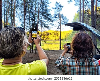 Friends enjoy a peaceful lakeside view while taking photos of the vibrant landscape under a clear blue sky. - Powered by Shutterstock