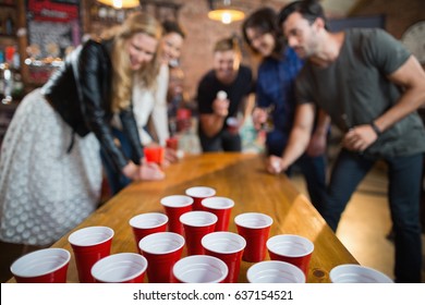 Friends enjoying beer pong game on table in bar
