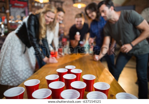 Friends enjoying\
beer pong game on table in\
bar