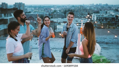 Friends Enjoying Cocktails At A Party. Group Of Happy People Having Fun, Dancing On A Rooftop