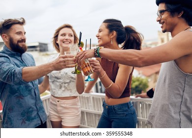 Friends Enjoying Cocktails At A Party. Friends Having Fun And Drinking Cocktails Outdoor On A Rooftop Get Together. Group Of Friends Toasting Drinks Outdoors.