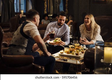 FRiends are enjoying drinks and food in a bar/restaurant. They are laughing and talking while eating burgers and drinking beer.