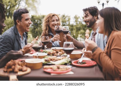 Friends Enjoying Outdoor Dinner - A group of friends aged 25-45 enjoying skewers and wine in the garden. A bearded man and a mature blonde woman toast during a pleasant summer evening.