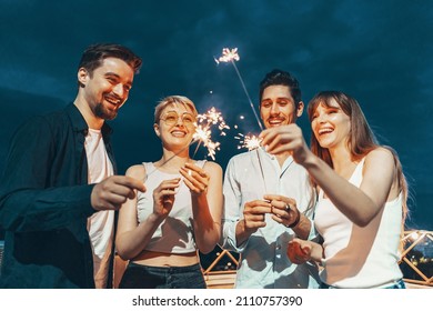 Friends enjoying a rooftop party and dancing with sparklers in hands - Powered by Shutterstock