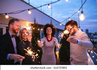 Friends Enjoying A Rooftop Party And Dancing With Sparklers In Hands.