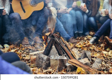 Friends enjoying singing songs, spending time together, have good mood, celebrating someone's birthday, spend sunny autumn day. Friendship concept. Company of young people are sitting around bonfire