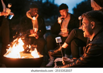 Friends enjoying s'mores and marshmallow together by the bonfire. Happy diverse friends, women and men at bonfire, friends outdoors, together at party, autumn party outdoors. - Powered by Shutterstock