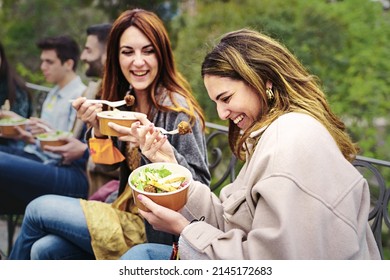 Friends enjoying take-away salads in eco-friendly paper bowls while chatting outdoors. - Powered by Shutterstock