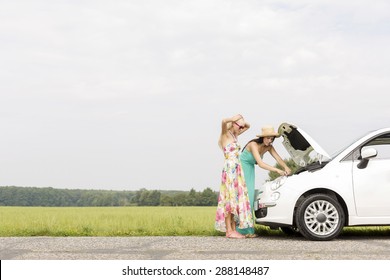 Friends examining broken down car on country road against clear sky - Powered by Shutterstock