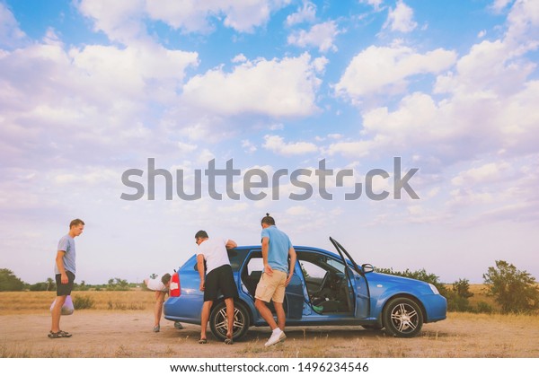 Friends examining broken down car on sunny day\
at roadtrip vacation excursion. Group of young people on road trip\
repair breakdown rent car on sea beach. Adventure lifestyle travel\
friendship concept.